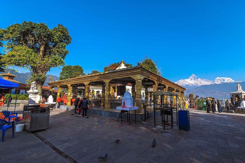A traditional temple with ornate architecture, a large tree, and a mountainous backdrop. 3