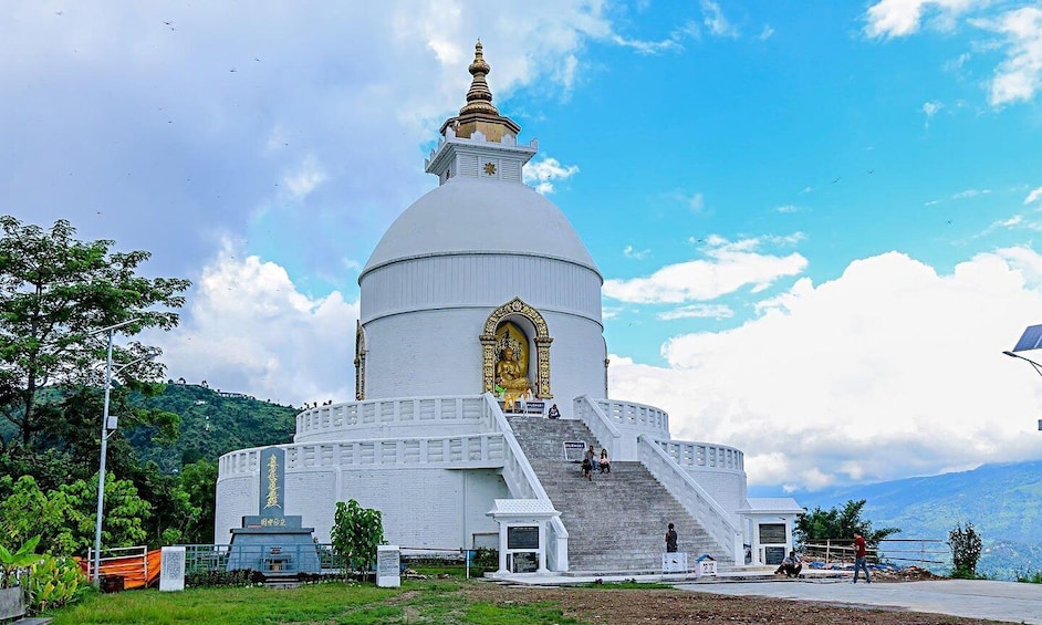 A white stupa with a golden statue, surrounded by stairs and greenery. 5