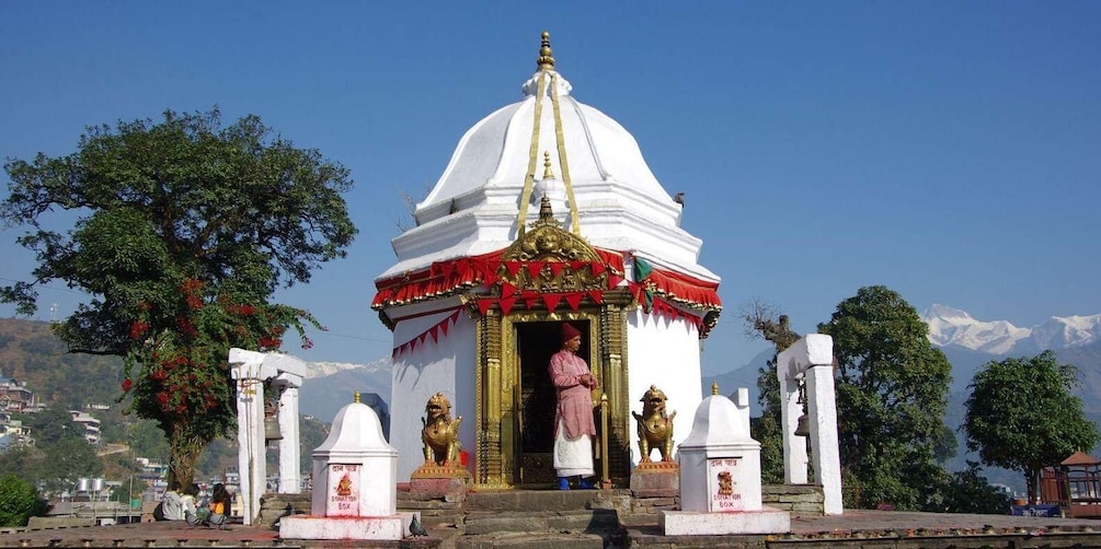 A white temple with a golden statue in front, surrounded by trees and mountains in the background. 1