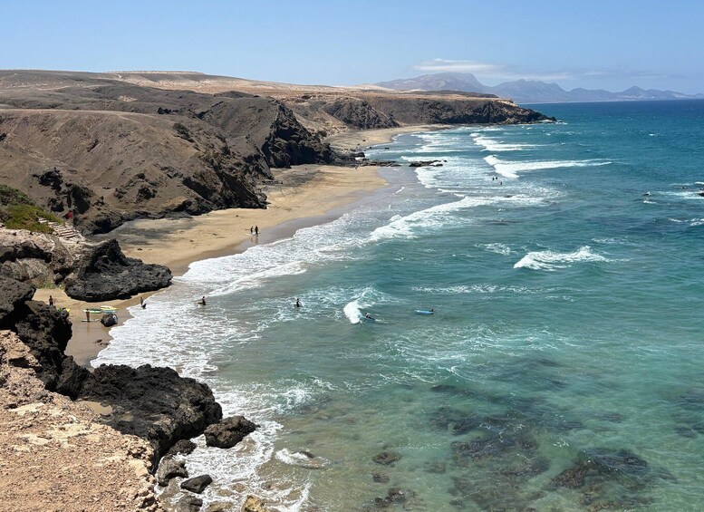 A coastal landscape with rocky cliffs, clear turquoise waters, and a sandy beach. 4