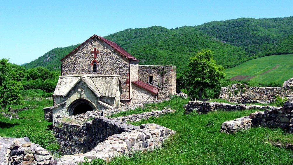 A stone church with a red roof and a cross, surrounded by lush green hills and fields. 3