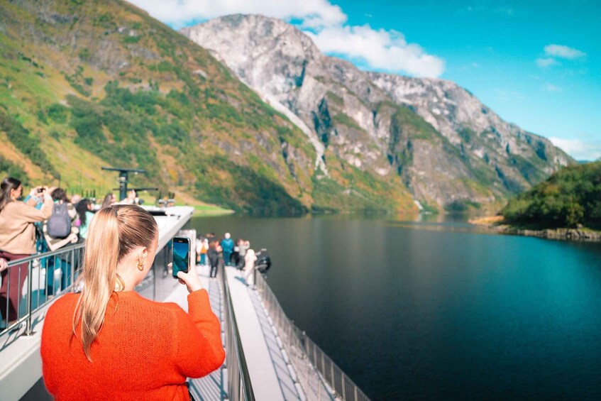 A person taking a photo on a boat with a mountainous landscape in the background. 1