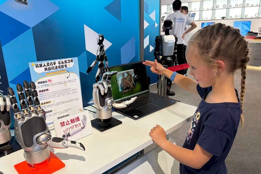 A child interacting with a robotic arm on a laptop, with a signboard in the background. 4