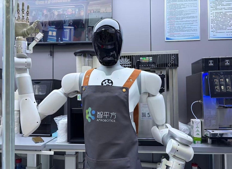 A humanoid robot wearing a black helmet and a grey apron with a logo, standing in a modern kitchen with coffee machines and a menu board in the background. 5