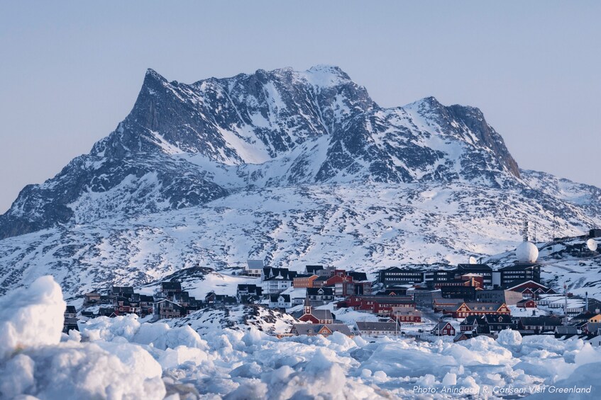 A snow-covered town with buildings and a mountain in the background. 1