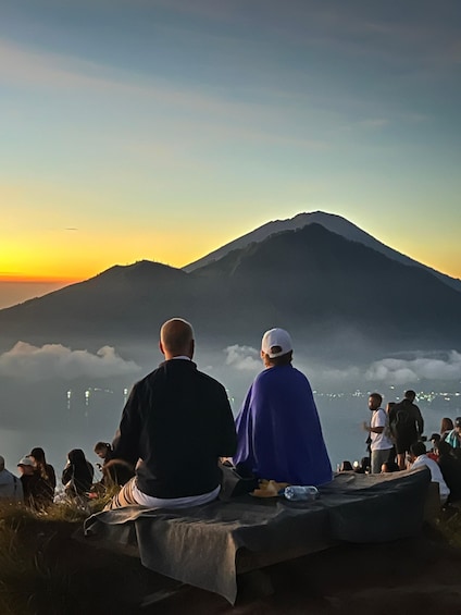 Two people sitting on a blanket overlooking a mountain at sunset. 5