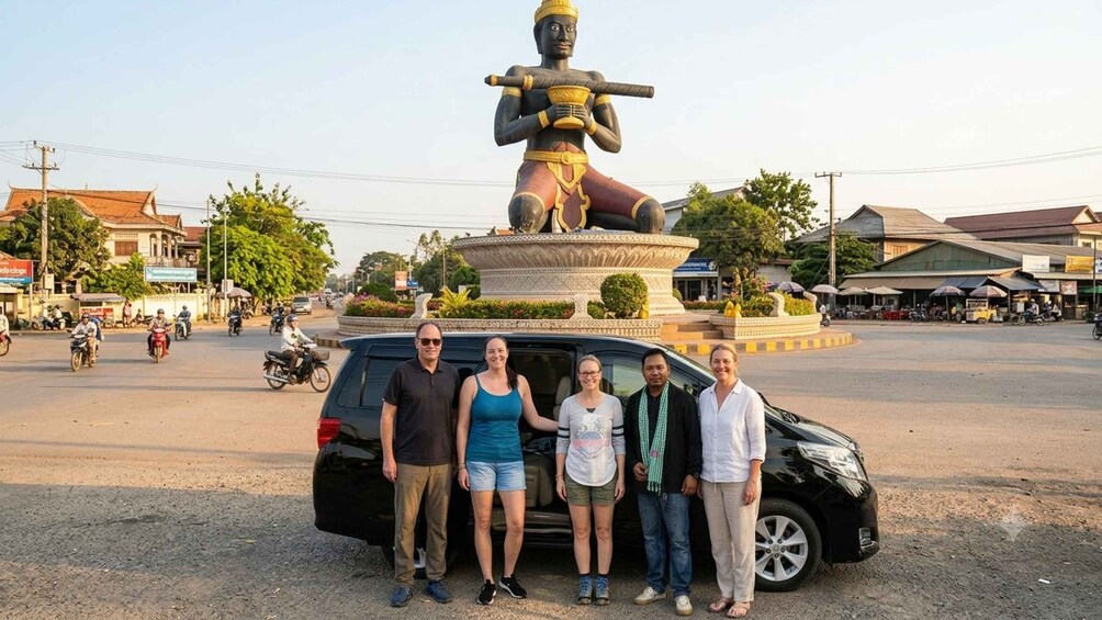A group of people standing in front of a large statue on a roundabout with buildings and vehicles in the background. 3