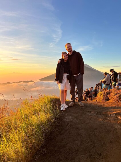A couple standing on a mountain trail with a view of a volcano in the background. 4