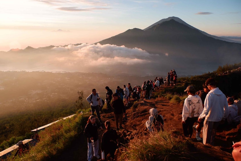 A group of people hiking on a mountain trail with a volcano in the background. 1