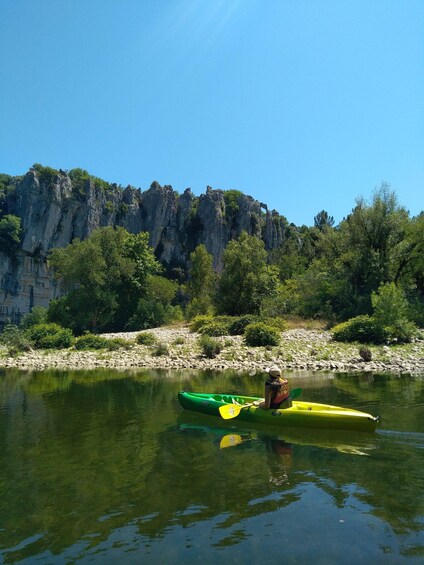 A kayaker in a green kayak on a calm river with rocky cliffs in the background. 3