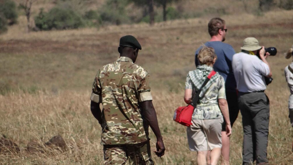 Una persona con abbigliamento mimetico militare cammina in un campo insieme ad altre persone, alcune delle quali portano macchine fotografiche. 4