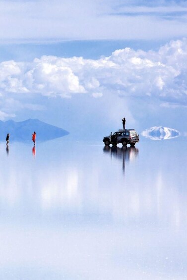 A vehicle on a reflective surface with two people standing in the distance. 1
