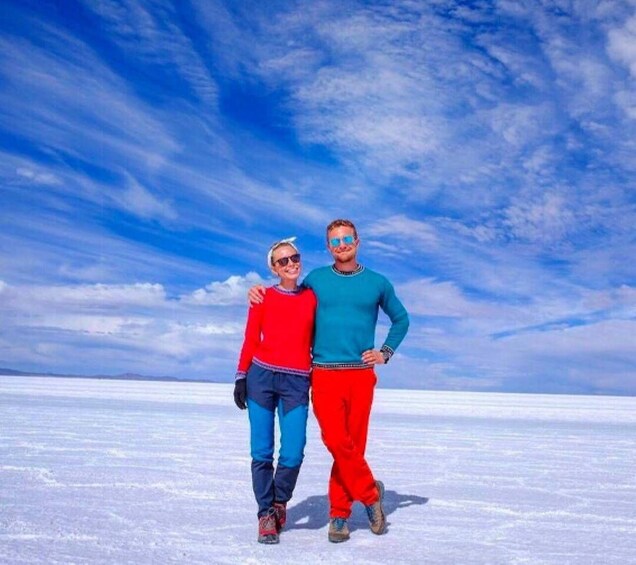 Two people standing on a flat, white surface with a blue sky and clouds in the background. 4