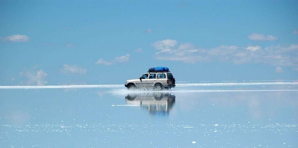 A white SUV driving on a frozen lake with a blue tarp on the roof. 5
