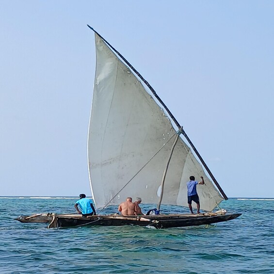 A sailboat with three people on board, one standing and two seated, sailing on calm waters. 5