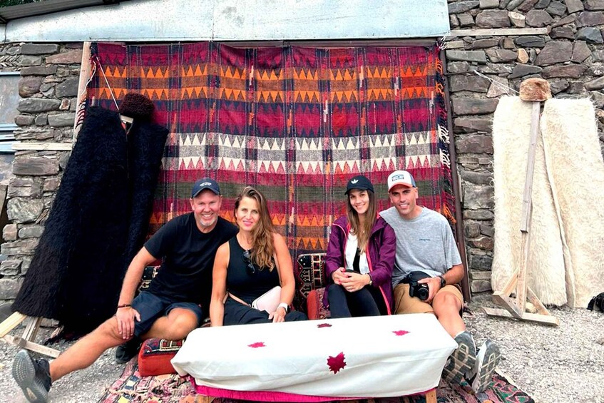 A group of people sitting in front of a patterned backdrop, with a table covered in a white cloth with red maple leaves. 3