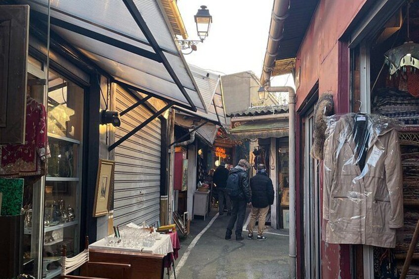 A narrow alley with shops on either side, a person walking, and a hanging coat. 3