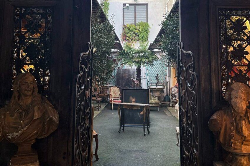 A courtyard with a central table, surrounded by statues and ornate doors. 2