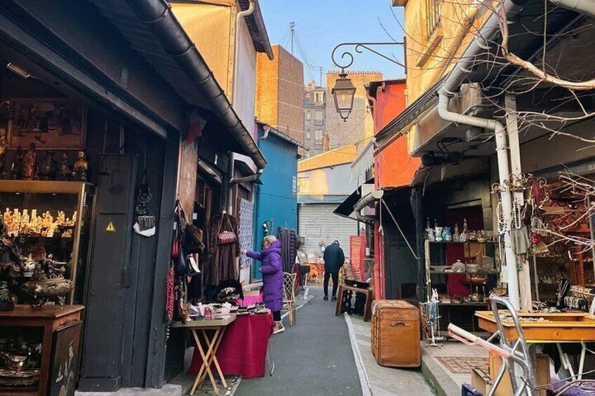 A narrow street with shops on either side, a person in purple, and a suitcase on the ground. 4
