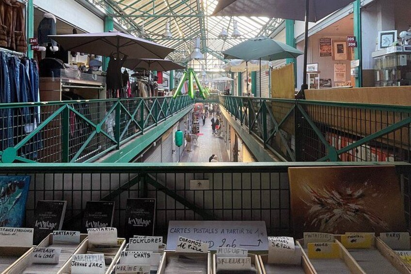 An indoor market with a green metal railing, various stalls, and signs in multiple languages. 4