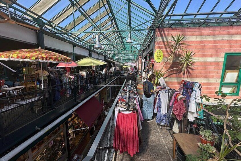 An indoor market with stalls selling clothes and plants. 2