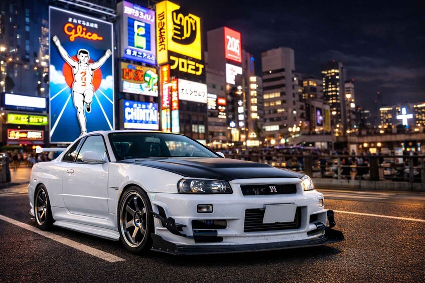 A white sports car parked on a city street at night with illuminated billboards and buildings in the background. 2
