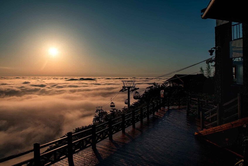 A wooden boardwalk overlooking a sea of clouds with a sun setting in the background. 2