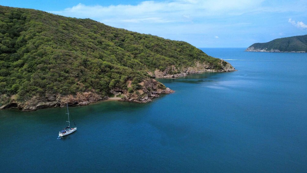 A sailboat on a calm sea with a green forested island in the background. 2