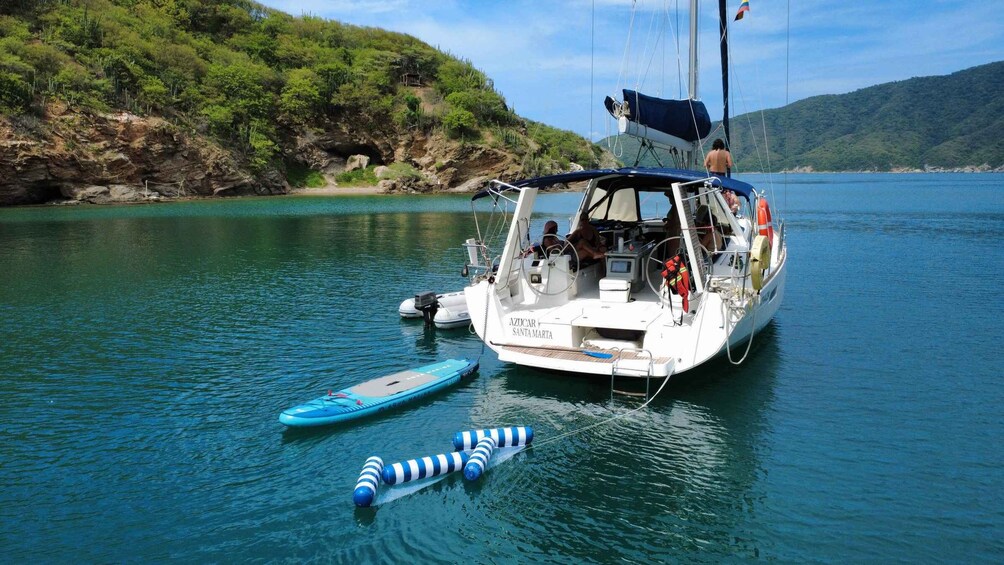 A sailboat named 'AZUCAR SANTA MARTA' anchored near a rocky shore with a clear blue water body. 3
