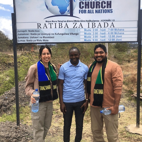 Three people standing in front of a signboard with a globe and text. 2