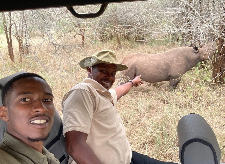 Two people in safari vehicles observing a large animal in a dry, wooded area. 1