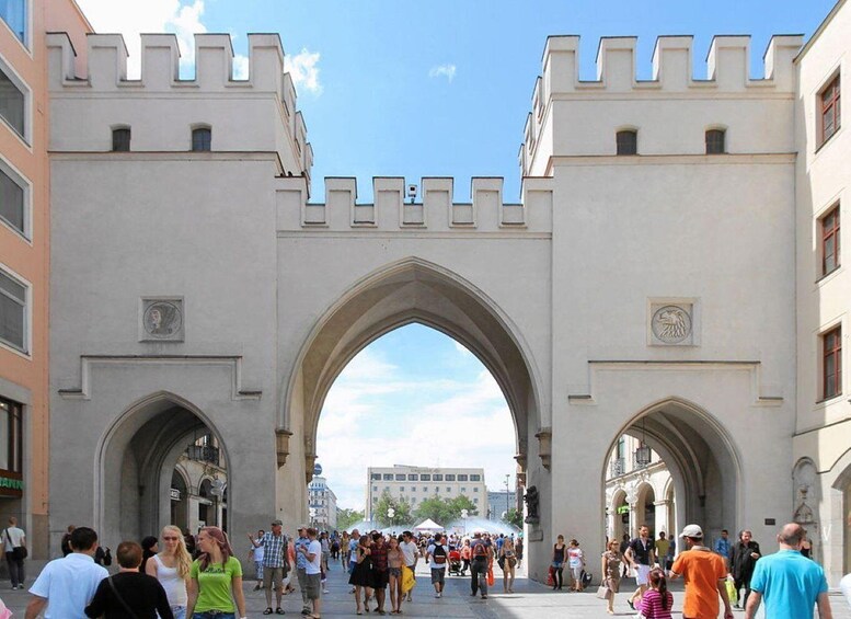 A large arched gateway with battlements, surrounded by people walking. 4
