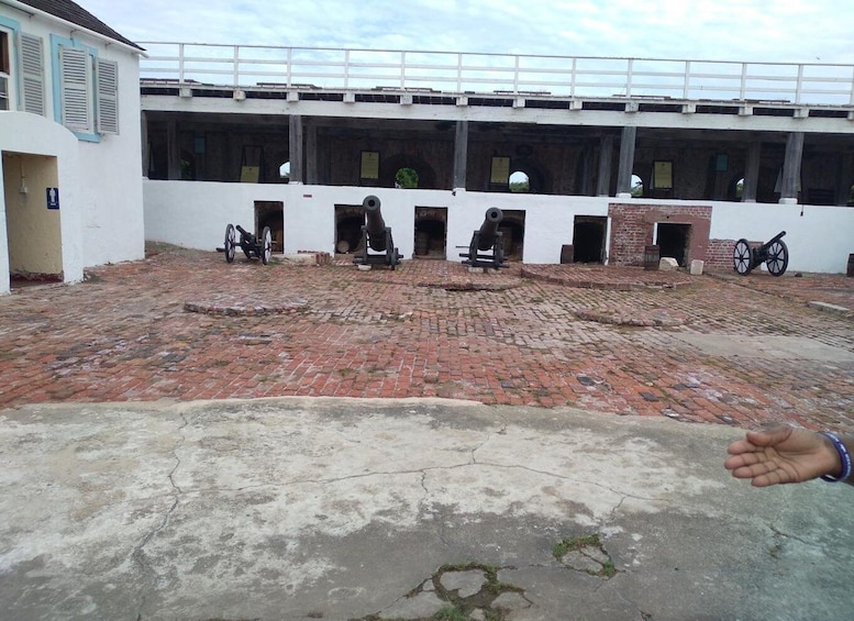 A historical building with cannons, a brick courtyard, and a white fence. 1