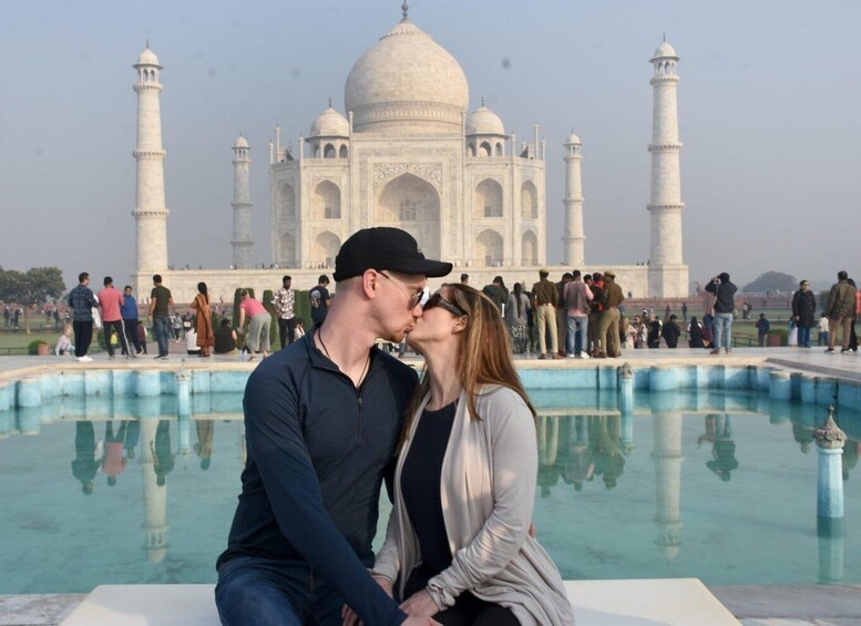 A couple sitting in front of the Taj Mahal with a reflection in the pool. 5
