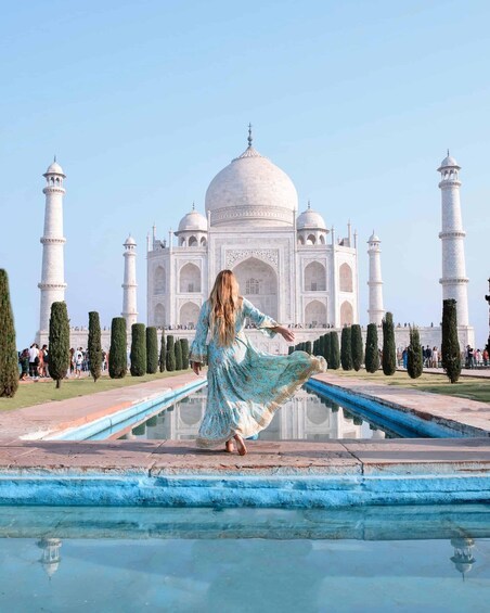 A person in a flowing dress standing in front of the Taj Mahal, with its reflection visible in the water. 2