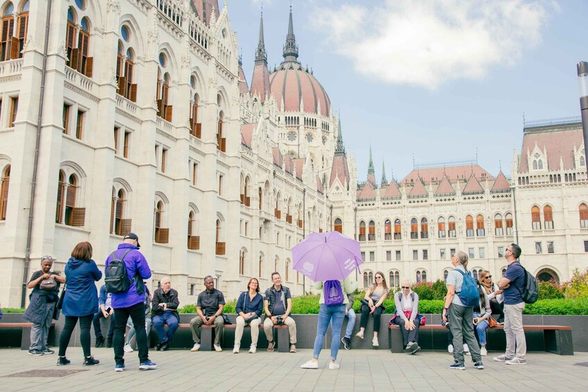 A group of people sitting on benches in front of a large, ornate building with a dome and spires. 4