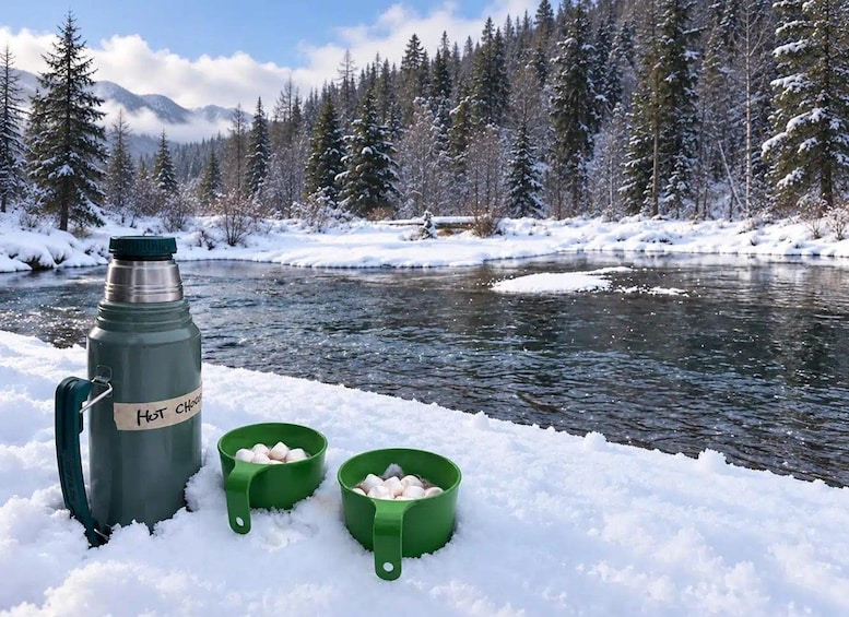 A thermos labeled 'HOT CHOCOLATE' and two green cups filled with marshmallows on a snowy riverbank. 5