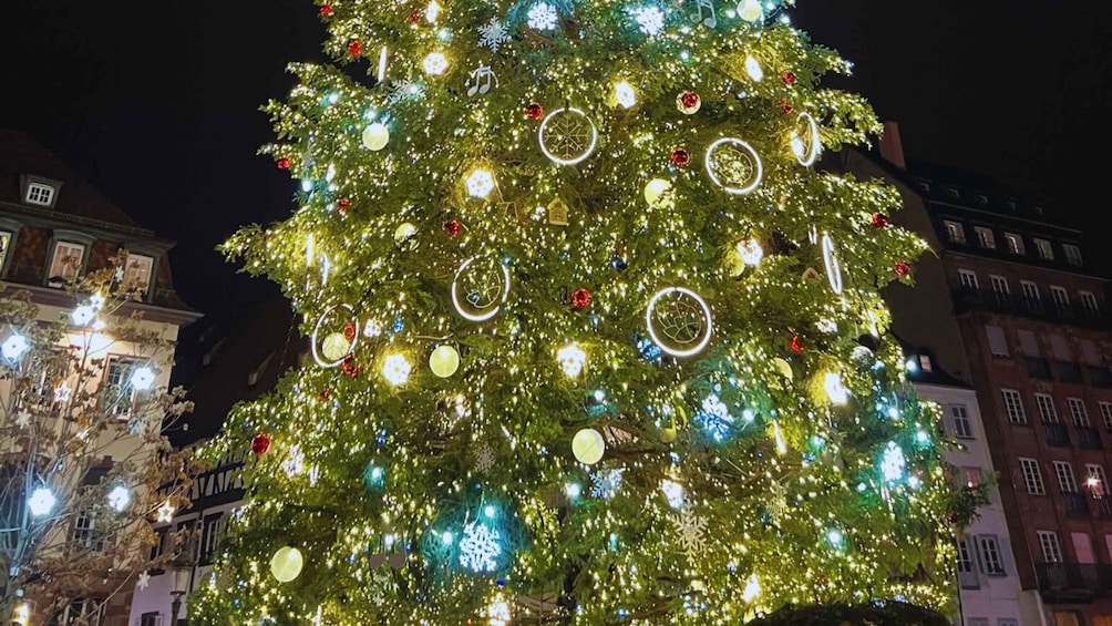 A large Christmas tree adorned with lights and ornaments, set against a cityscape at night. 4