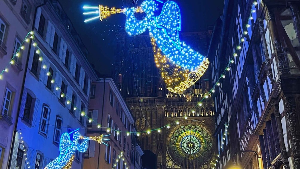 Illuminated figures of a mermaid and a fish, a cathedral with a large circular stained glass window, and string lights along the street. 3