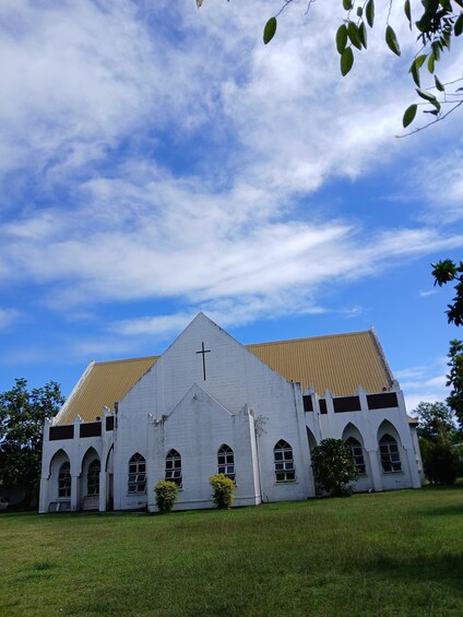 A white church with a cross on the front, surrounded by grass and trees. 2
