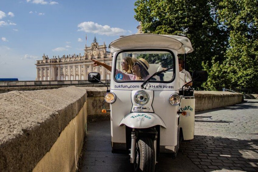 A tuk-tuk parked on a cobblestone path with a historic building in the background. 1