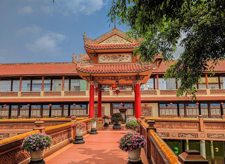 Un pavillon chinois traditionnel, doté d’un toit et de colonnes richement décorés, est entouré d’une cour où l’on trouve des plantes en pot. En arrière-plan, on aperçoit un bâtiment dont le toit est recouvert de tuiles. 2