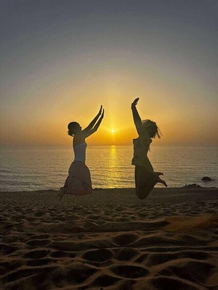 Two people jumping on a beach with the sun setting in the background. 1