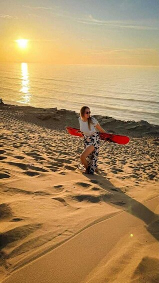 A person standing on a sandy beach holding a red kayak, with the sun setting in the background. 5