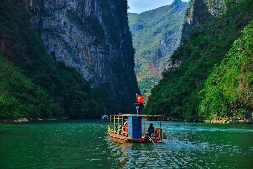 A boat with a Vietnamese flag on a river surrounded by steep cliffs. 1
