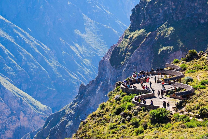 A winding stone pathway with people walking along it, surrounded by steep cliffs and sparse vegetation. 1