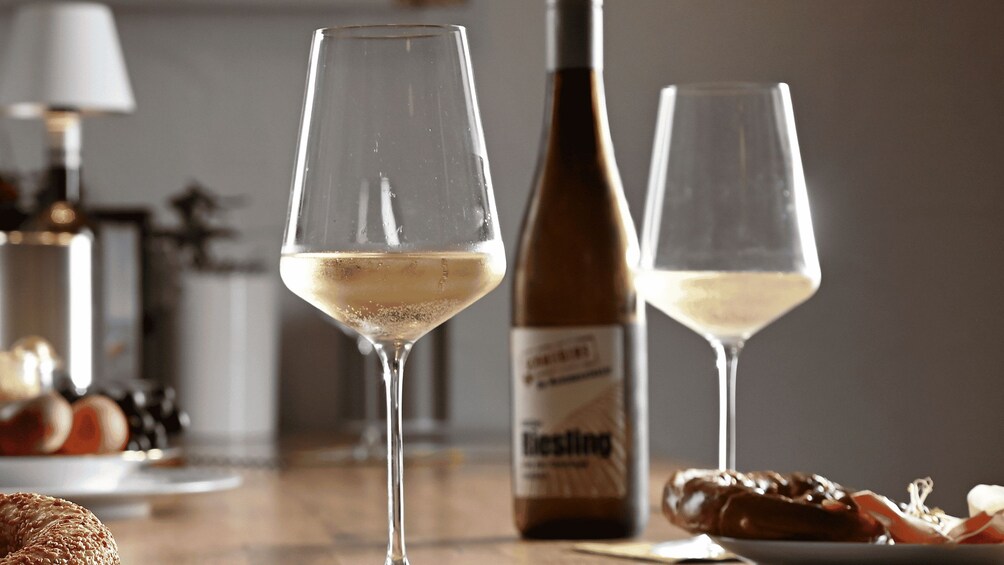 Two wine glasses with a bottle of Riesling wine and some food items on a table. 5