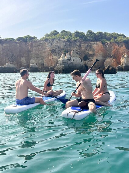 Four people on paddleboards in calm waters with rocky cliffs in the background. 4