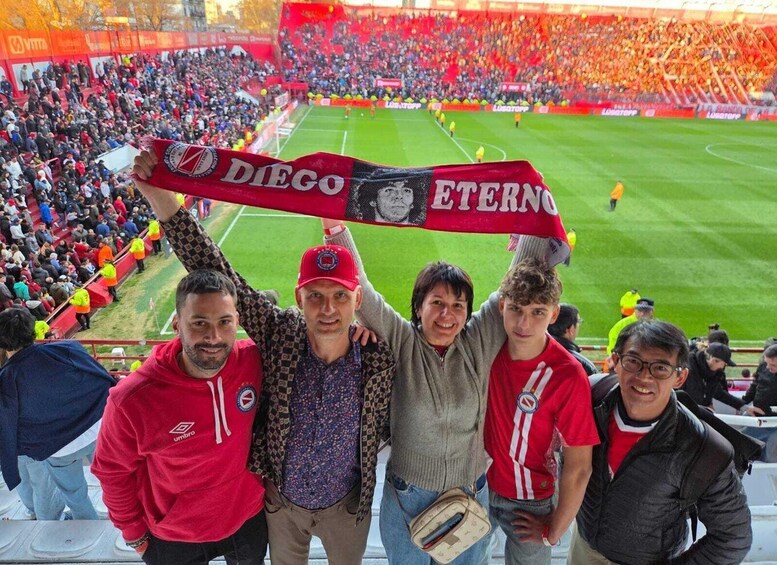 A group of people holding a Diego Eterno scarf at a football stadium. 2