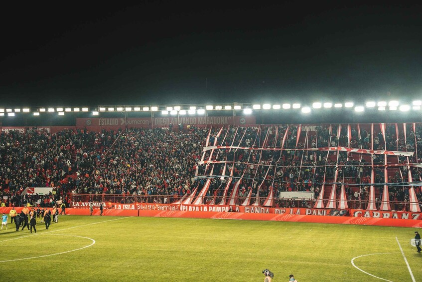 A football stadium with a large crowd, floodlights, and advertising banners. 5